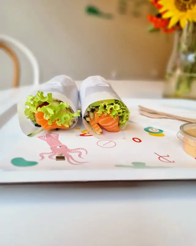Dwie niekrojone rolki sushi z sałatą i łososiem na kolorowej tacce